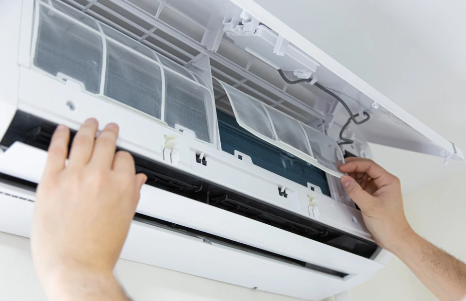 Technicien effectuant la maintenance d'un climatiseur mural intérieur, les mains positionnées pour retirer ou installer le filtre à air